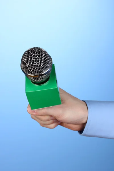 Male hand with microphone on blue background — Stock Photo, Image