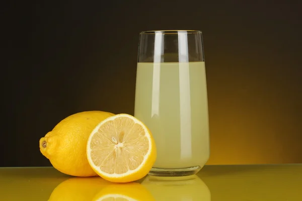 Delicioso zumo de limón en vaso y limones al lado sobre fondo naranja oscuro — Foto de Stock