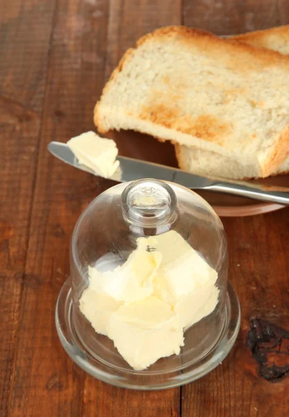 Mantequilla en platillo de vidrio con tapa de vidrio y pan fresco, sobre fondo de madera — Foto de Stock