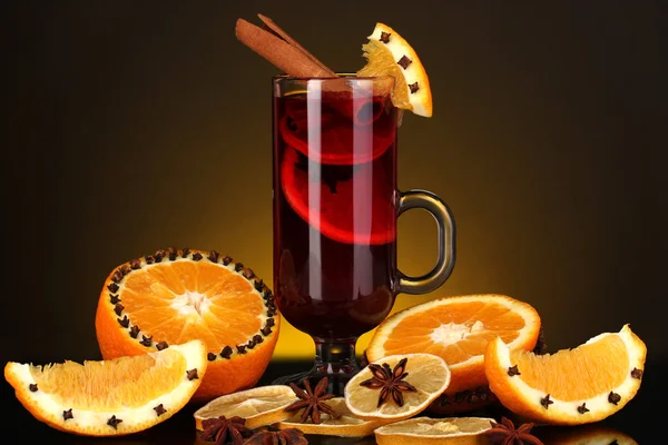 Duftender Glühwein im Glas mit Gewürzen und Orangen auf gelbem Hintergrund — Stockfoto