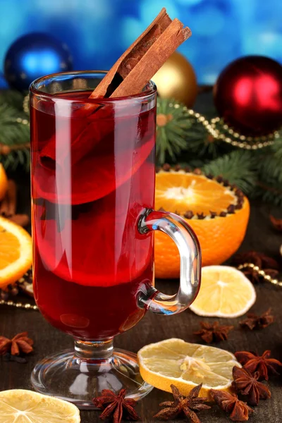 Fragrant mulled wine in glass with spices and oranges around on wooden table on blue background — Stock Photo, Image