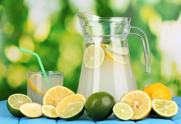 Citrus limonade in werper en glas van citrus rond op natuurlijke houten tafel op blauwe achtergrond — Stockfoto