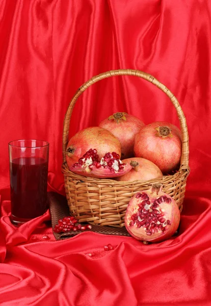Zralé granátová jablka na košík s sklenici šťávy z granátového jablka na červenou látkou pozadí — Stock fotografie