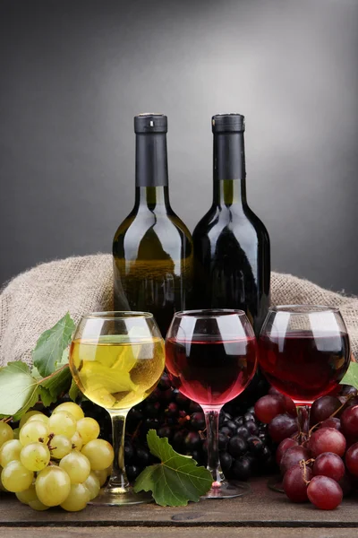 Flessen en glazen wijn en druiven op grijze achtergrond — Stockfoto