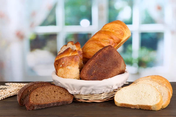 Färskt bröd i korg på träbord på fönsterbakgrund — Stockfoto