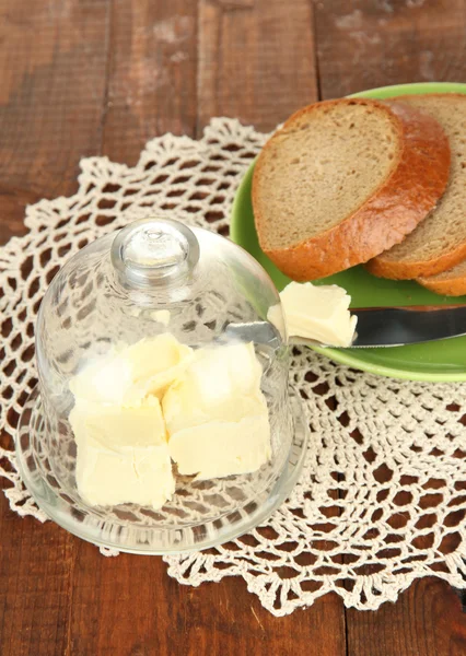 Butter on glass saucer with glass cover and fresh bread, on wooden background — Stock Photo, Image