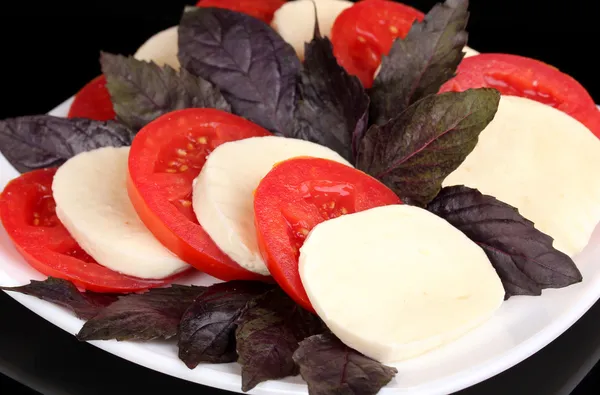 Tasty mozzarella with tomatoes on plate isolated on black — Stock Photo, Image