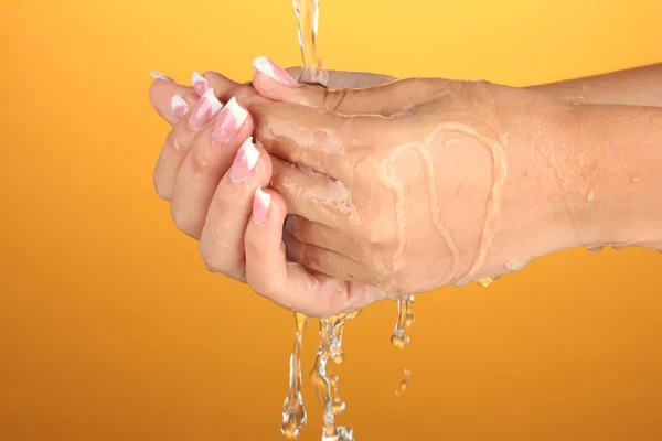 Lavarse las manos de la mujer sobre fondo naranja de cerca —  Fotos de Stock
