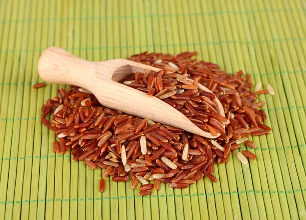 Riz rouge dans une cuillère en bois sur tapis de bambou — Photo