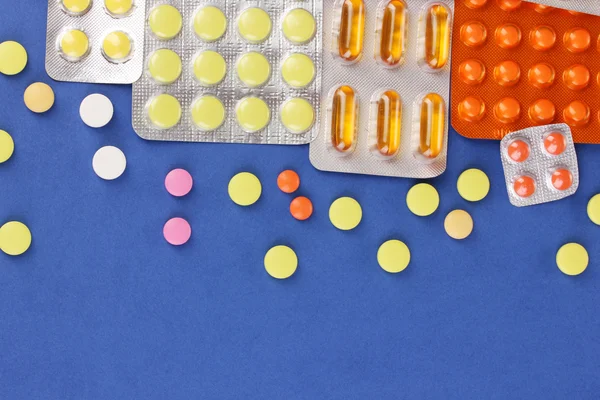 Cápsulas y pastillas empaquetadas en ampollas sobre fondo azul —  Fotos de Stock