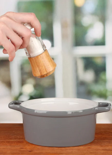 Hand adding salt using salt shaker on bright background — Stock Photo, Image