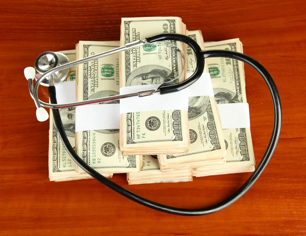 Healthcare cost concept: stethoscope and dollars on wooden background — Stock Photo, Image