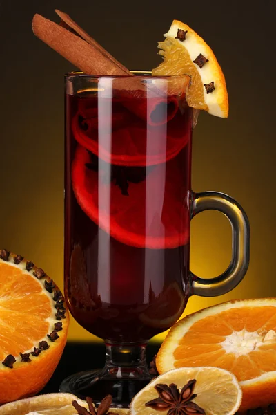 Geurige glühwein in glas met specerijen en sinaasappelen rond op gele achtergrond — Stockfoto