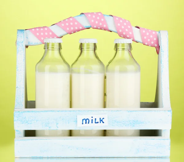 Milch in Flaschen in Holzkiste auf grünem Hintergrund — Stockfoto