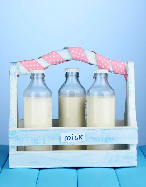 Milch in Flaschen in Holzkiste auf blauem Holztisch auf blauem Hintergrund — Stockfoto