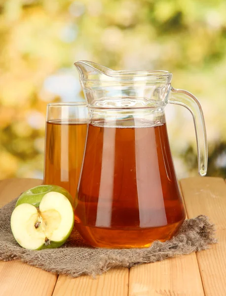 Vol glas en kruik van appelsap en appels op houten tafel buiten — Stockfoto