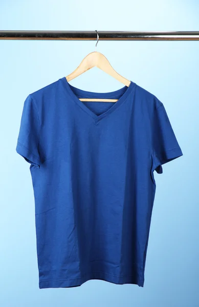 Camiseta en percha de madera, sobre fondo azul — Foto de Stock