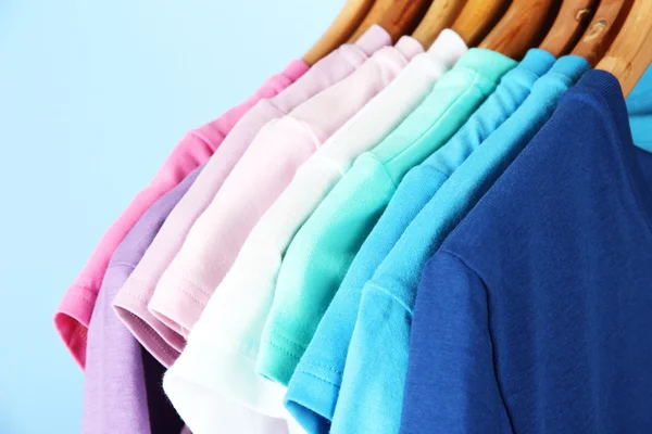 Varietà di camicie casual su appendini di legno, su sfondo blu — Foto Stock