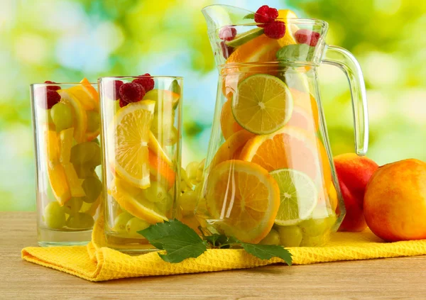Jar and glasses with citrus fruits and raspberries, on green background — Stock Photo, Image