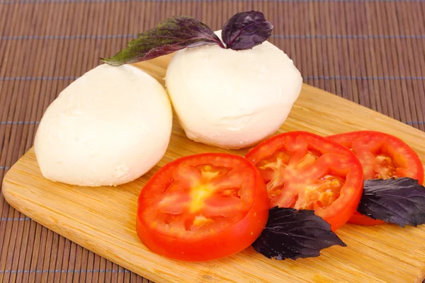 Mussarela saborosa com tomates em tábua de corte no tapete — Fotografia de Stock