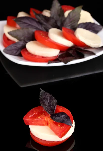 Tasty mozzarella with tomatoes on plate isolated on black — Stock Photo, Image