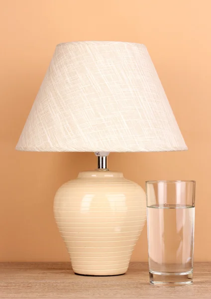 Tischlampe und Glas Wasser auf beigem Hintergrund — Stockfoto