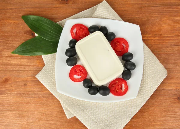 Feta cheese on plate decorated with olives and tomatoes on wooden table close-up — Stock Photo, Image