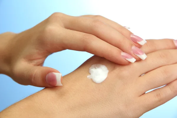 Beautiful woman hands with cream, on blue background — Stock Photo, Image