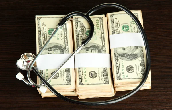 Healthcare cost concept: stethoscope and dollars on wooden background — Stock Photo, Image