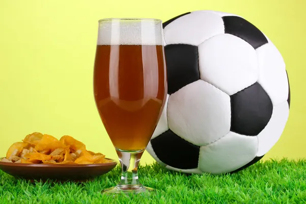 Copo de cerveja com bola de futebol na grama no fundo verde — Fotografia de Stock