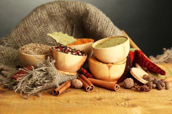 Skålar och skedar med kryddor, på träbord på grå bakgrund — Stockfoto