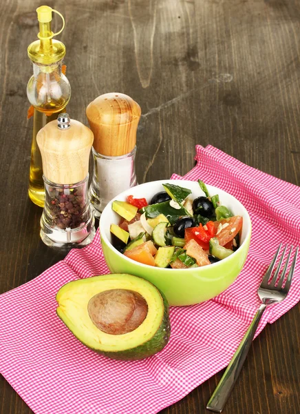 Tasty avocado salad in bowl surrounded by spices on wooden table close-up — Stock Photo, Image