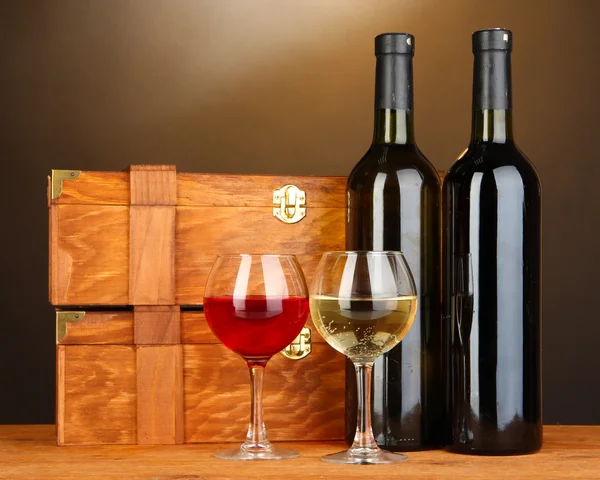 Wooden cases with wine bottles on wooden table on brown background — Stock Photo, Image