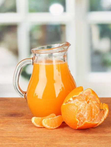 Full jug of tangerine juice, on wooden table on bright background — Stock Photo, Image