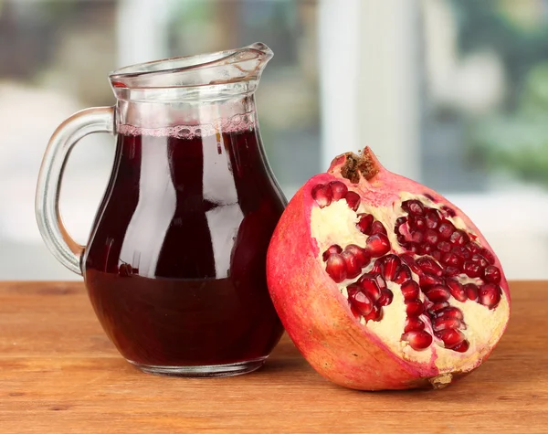 Full jug of pomegranate juice,on wooden table on bright background — Stock Photo, Image