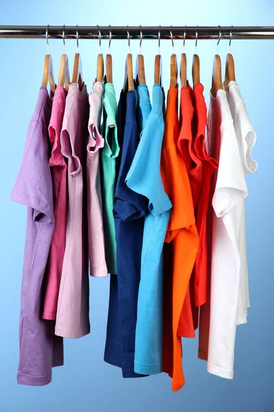 Verscheidenheid van casual shirts op houten hangers, op blauwe achtergrond — Stockfoto