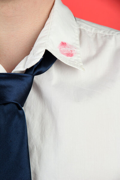 Lipstick kiss on shirt collar of man, on red background
