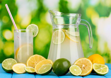 narenciye limonata sürahi ve bardak narenciye çevresinde doğal ahşap masa mavi zemin üzerinde