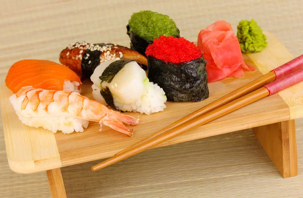 Köstliches Sushi auf Holzbrett auf Bambusmatte serviert — Stockfoto