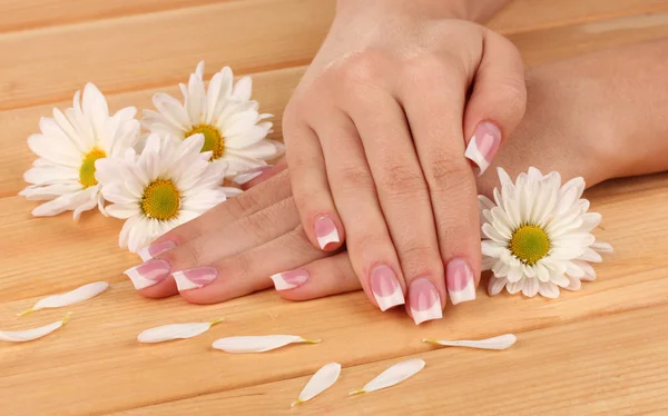 Mãos de mulher com manicure francês e flores em fundo de madeira — Fotografia de Stock