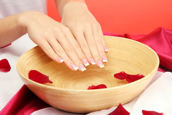 Woman hands with wooden bowl of water with petals, on red background — Stock Photo, Image