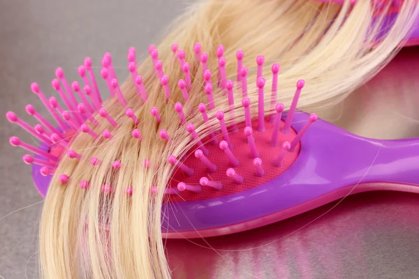 Blond curls brushing comb on metalic background — Stock Photo, Image