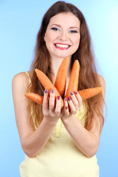 Mulher bonita com cenoura no fundo azul — Fotografia de Stock