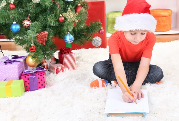 Menino em chapéu de Papai Noel escreve carta para Papai Noel — Fotografia de Stock