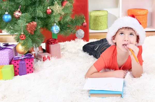 Menino em chapéu de Papai Noel escreve carta para Papai Noel — Fotografia de Stock