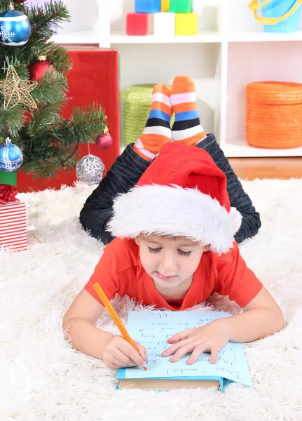 Маленький мальчик в шляпе Санты пишет письмо Санта Клаусу — стоковое фото