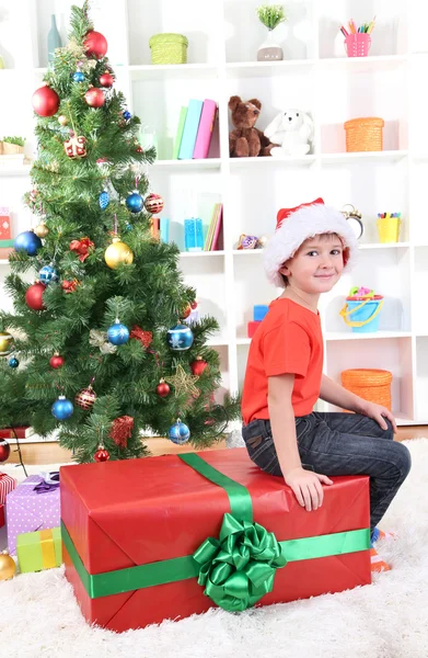 Criança em chapéu de Santa perto da árvore de Natal com grande presente — Fotografia de Stock