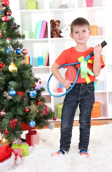 Liten pojke står nära julgran med badmintonracketar — Stockfoto