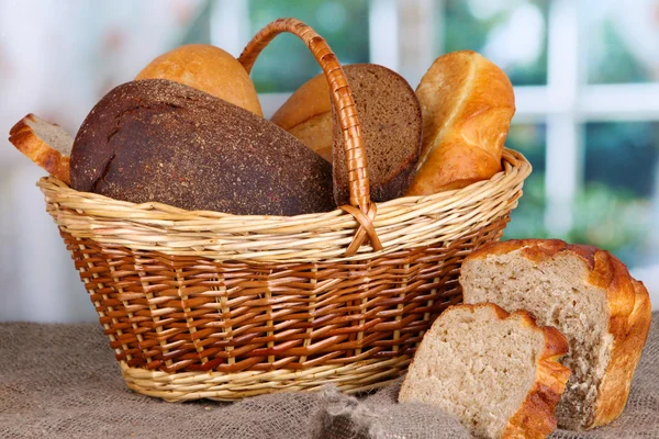 Fresh bread in basket on wooden table on window background — Stock Photo, Image