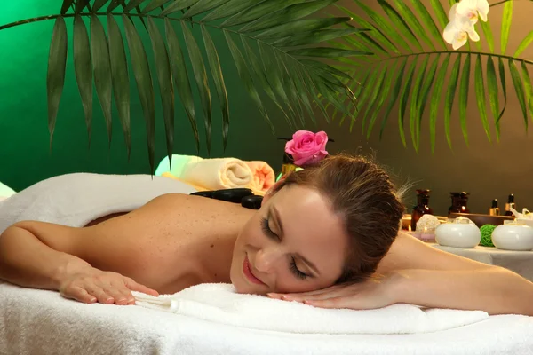 Hermosa joven en el salón de spa con piedras de spa, sobre fondo verde —  Fotos de Stock